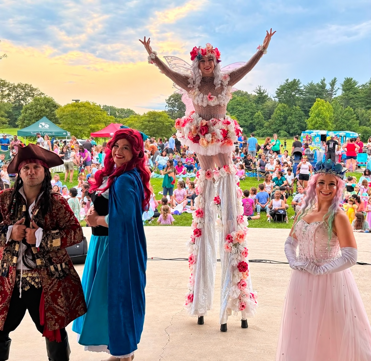 Beauty & The Beats cast with a flower costumed stilt walker and families at an outdoor festival